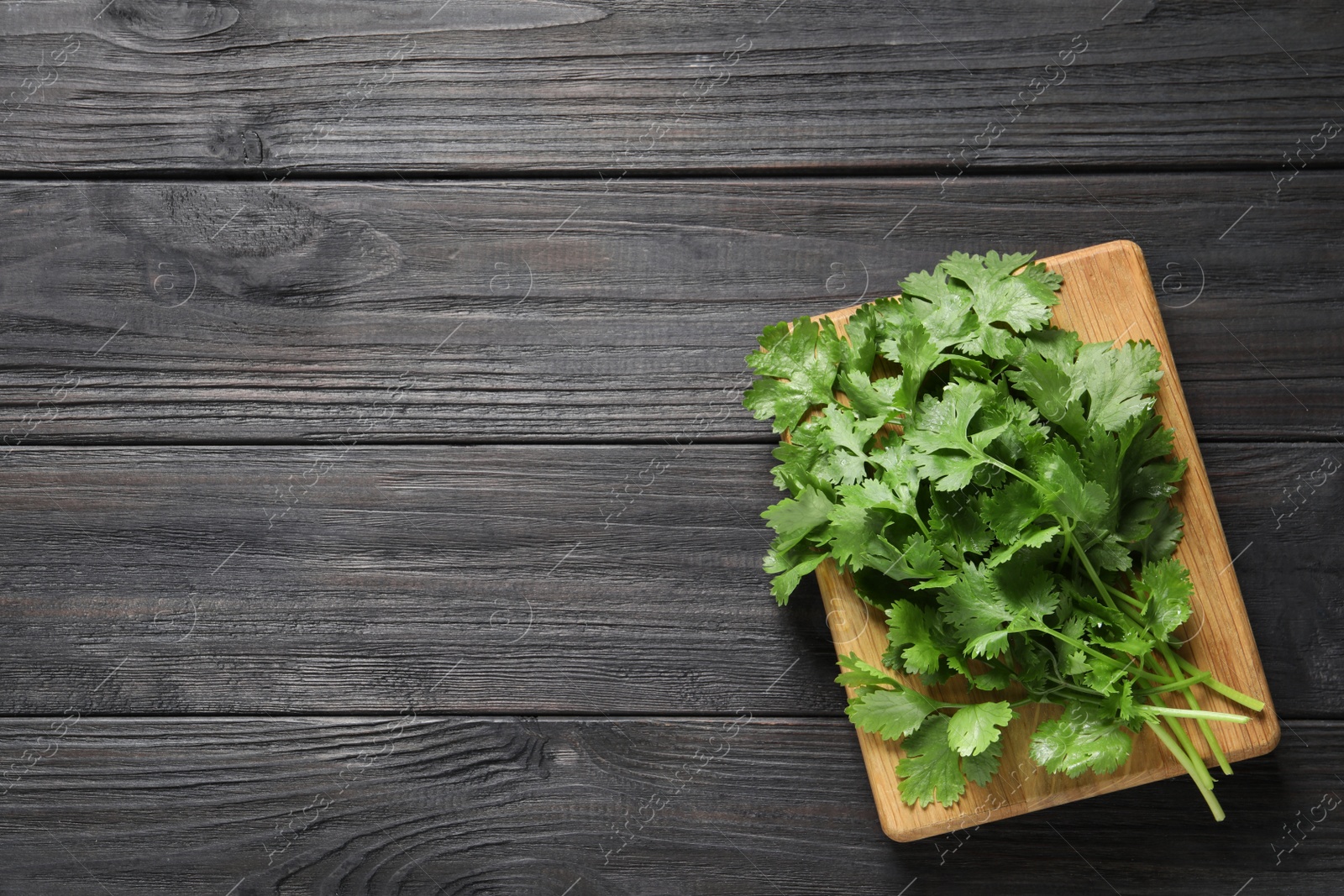 Photo of Bunch of fresh green cilantro and board on black wooden table, top view. Space for text