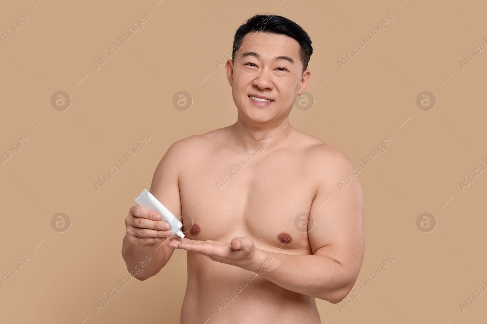 Photo of Handsome man applying body cream onto his hand on light brown background