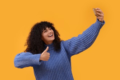 Photo of Beautiful young woman taking selfie with smartphone on orange background