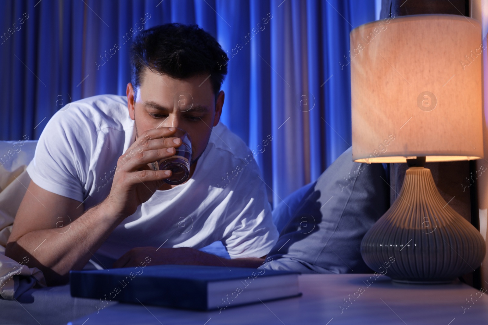 Photo of Sleepy man drinking water in dark room at night. Bedtime