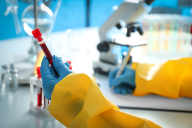 Scientist in chemical protective suit working with blood samples at table, closeup. Virus research