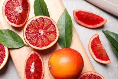 Photo of Ripe red oranges, green leaves and wooden board on light table, flat lay