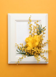 Photo of Beautiful floral composition with mimosa flowers and frame on orange background, top view