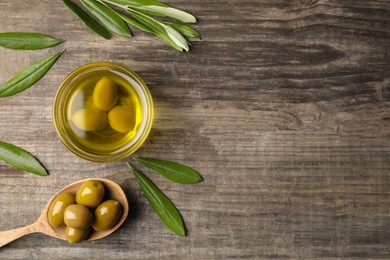 Photo of Cooking oil in bowl, olives and leaves on wooden table, flat lay. Space for text