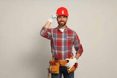Photo of Professional builder in hard hat with tool belt on light background