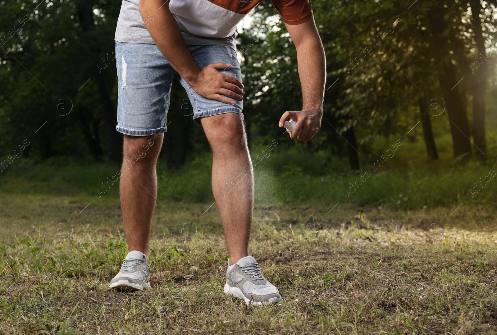 Photo of Man applying insect repellent on leg in park, closeup. Tick bites prevention