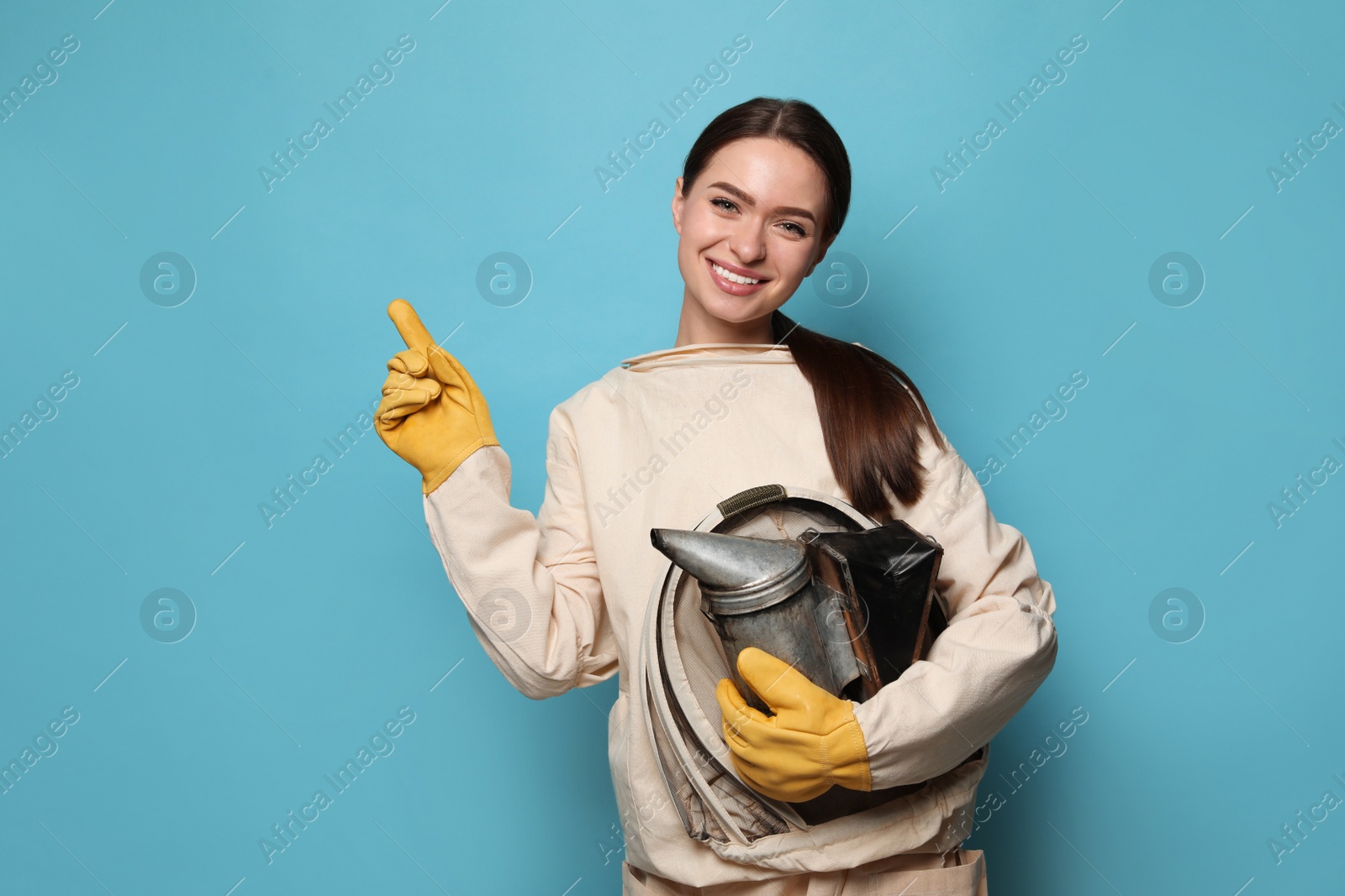 Photo of Beekeeper in uniform with smokepot pointing at something on light blue background