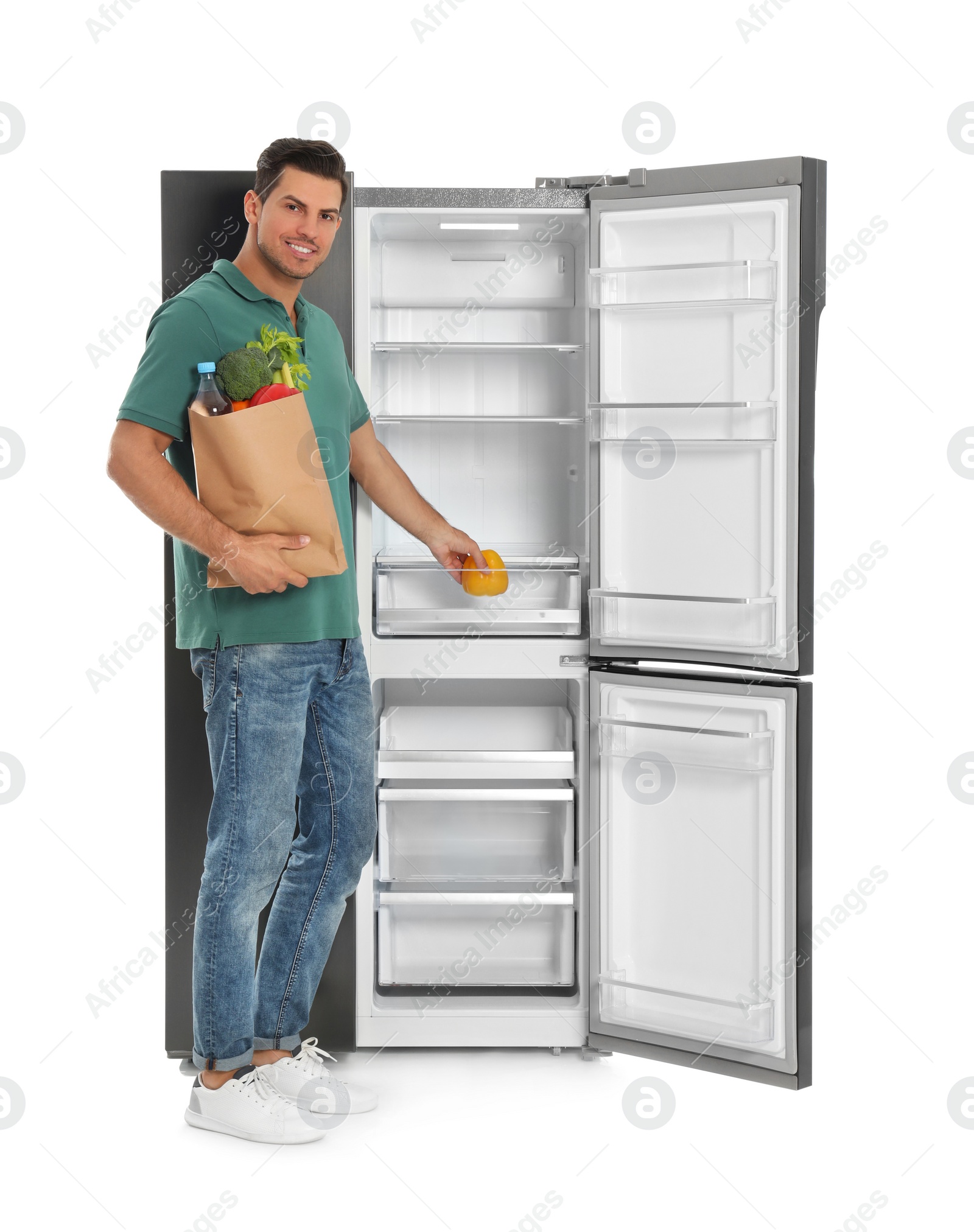 Photo of Man with bag of groceries near open empty refrigerator on white background