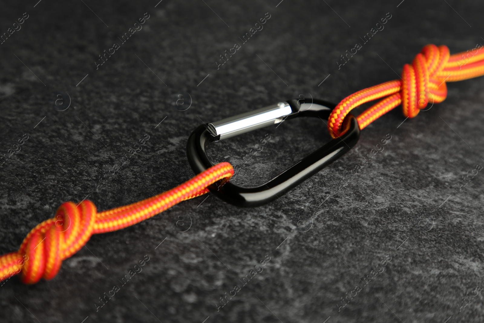 Photo of One metal carabiner with ropes on black table, closeup