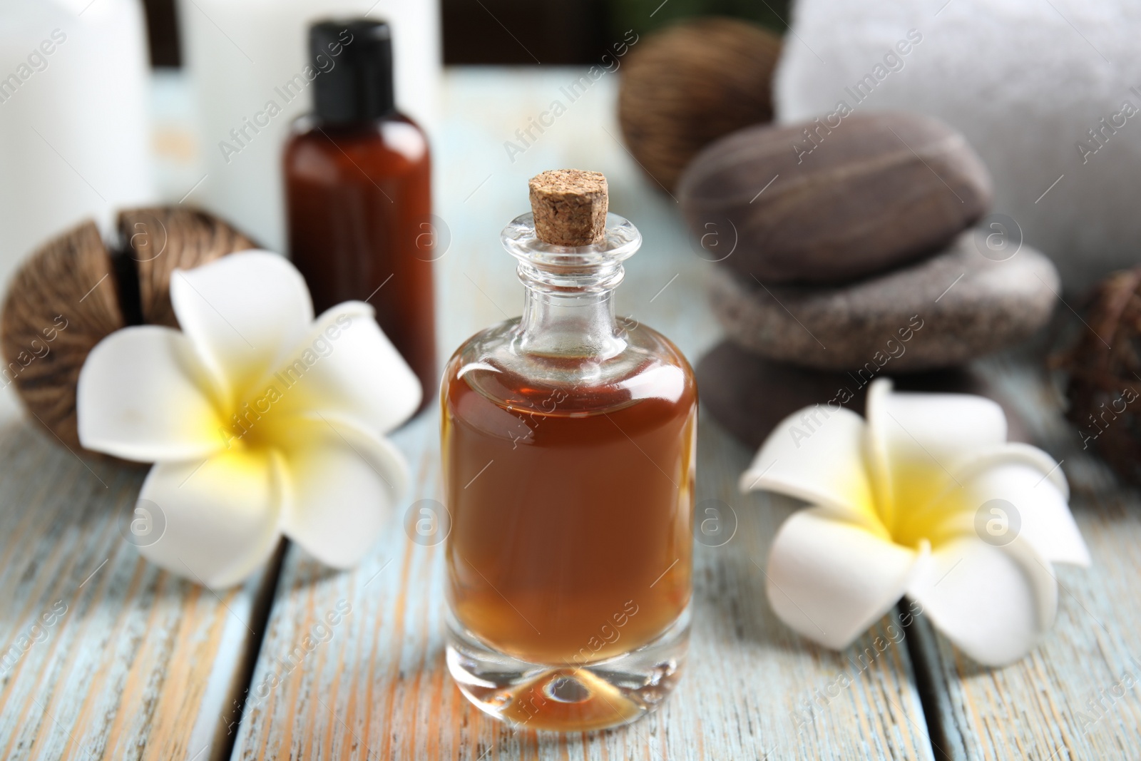 Photo of Composition with spa cosmetic and plumeria flowers on light wooden table, closeup