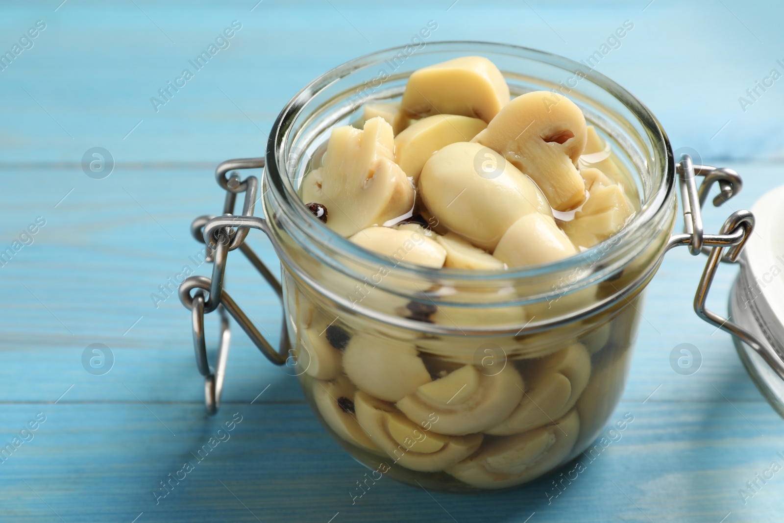 Photo of Delicious marinated mushrooms in glass jar on light blue wooden table, closeup