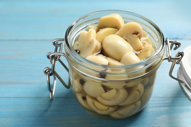 Photo of Delicious marinated mushrooms in glass jar on light blue wooden table, closeup