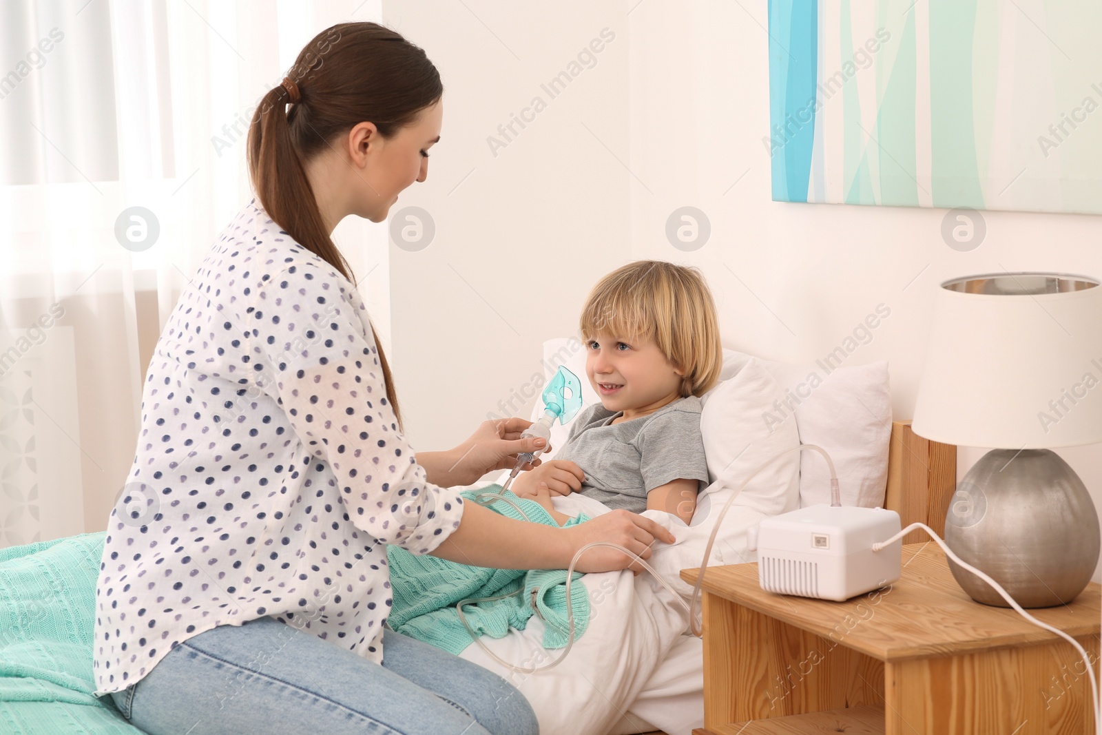 Photo of Mother helping her sick son with nebulizer inhalation in bedroom