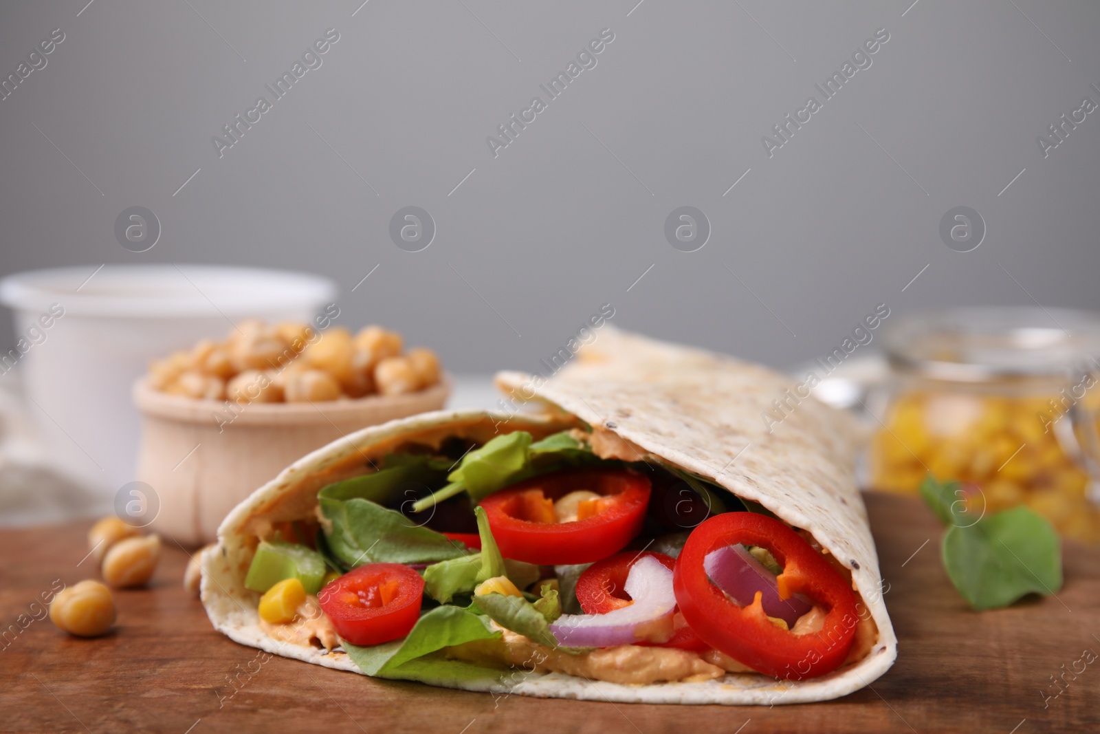 Photo of Delicious hummus wrap with vegetables on wooden board, closeup. Space for text