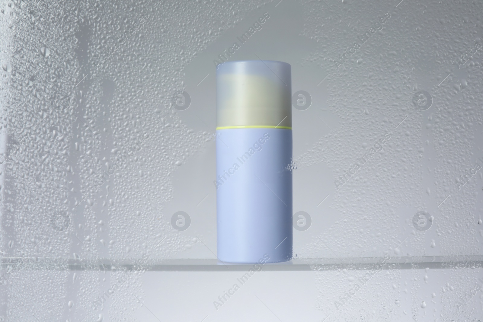 Photo of Bottle with moisturizing cream on light background, view through wet glass