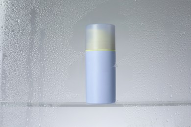 Bottle with moisturizing cream on light background, view through wet glass