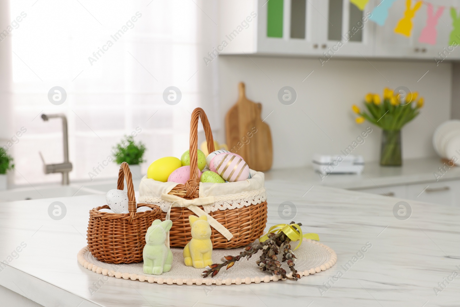 Photo of Wicker baskets with Easter eggs and willow twigs at white marble table in kitchen