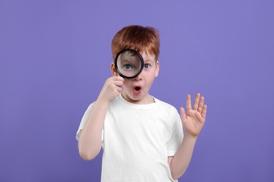 Photo of Surprised boy looking through magnifier glass on violet background