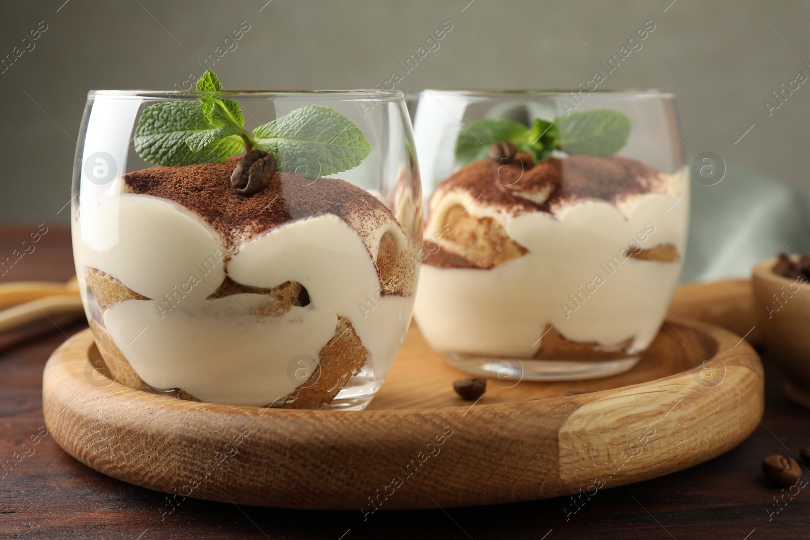 Photo of Delicious tiramisu in glasses, mint leaves and coffee beans on wooden table, closeup