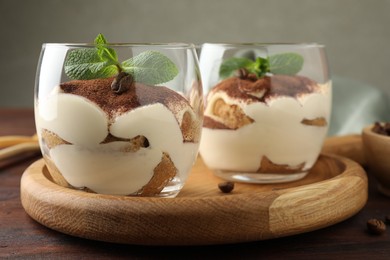 Photo of Delicious tiramisu in glasses, mint leaves and coffee beans on wooden table, closeup