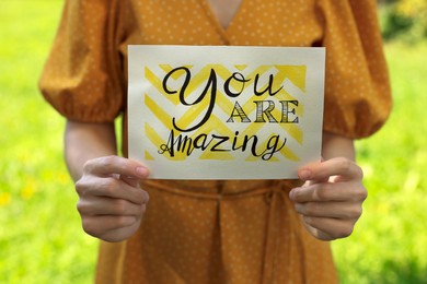 Woman holding card with phrase You Are Amazing outdoors, closeup