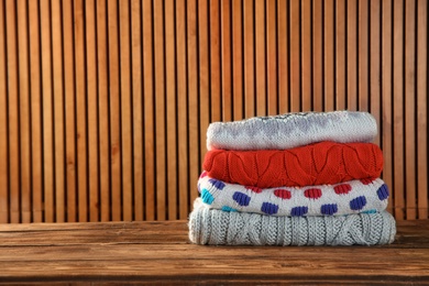 Photo of Pile of folded winter clothes on wooden table. Space for text