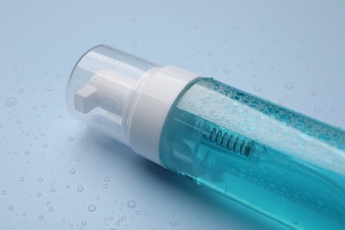 Photo of Wet bottle of face cleansing product on light blue background, closeup