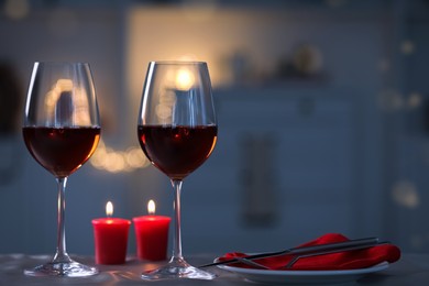 Romantic table setting with glasses of red wine and burning candles against blurred lights, space for text