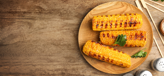 Image of Delicious grilled corn cobs and space for text on wooden table, flat lay. Banner design