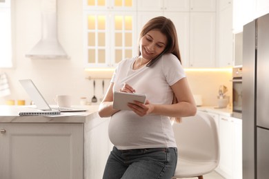 Pregnant woman working in kitchen at home. Maternity leave