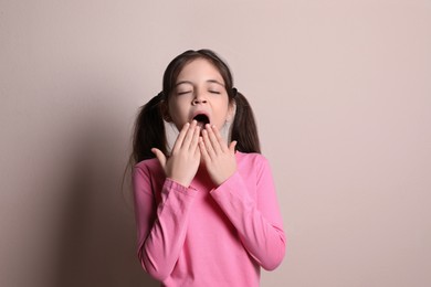 Photo of Sleepy little girl yawning on beige background