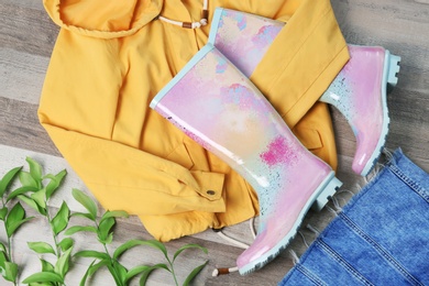 Photo of Pair of gumboots and jacket on wooden background, top view. Female shoes