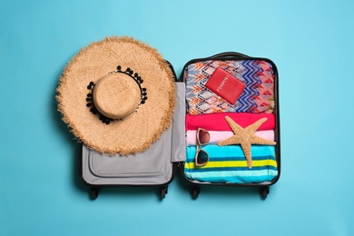 Photo of Open suitcase with traveler's belongings on color background, top view