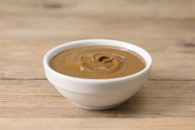 Photo of Delicious nut butter in bowl on wooden table, closeup