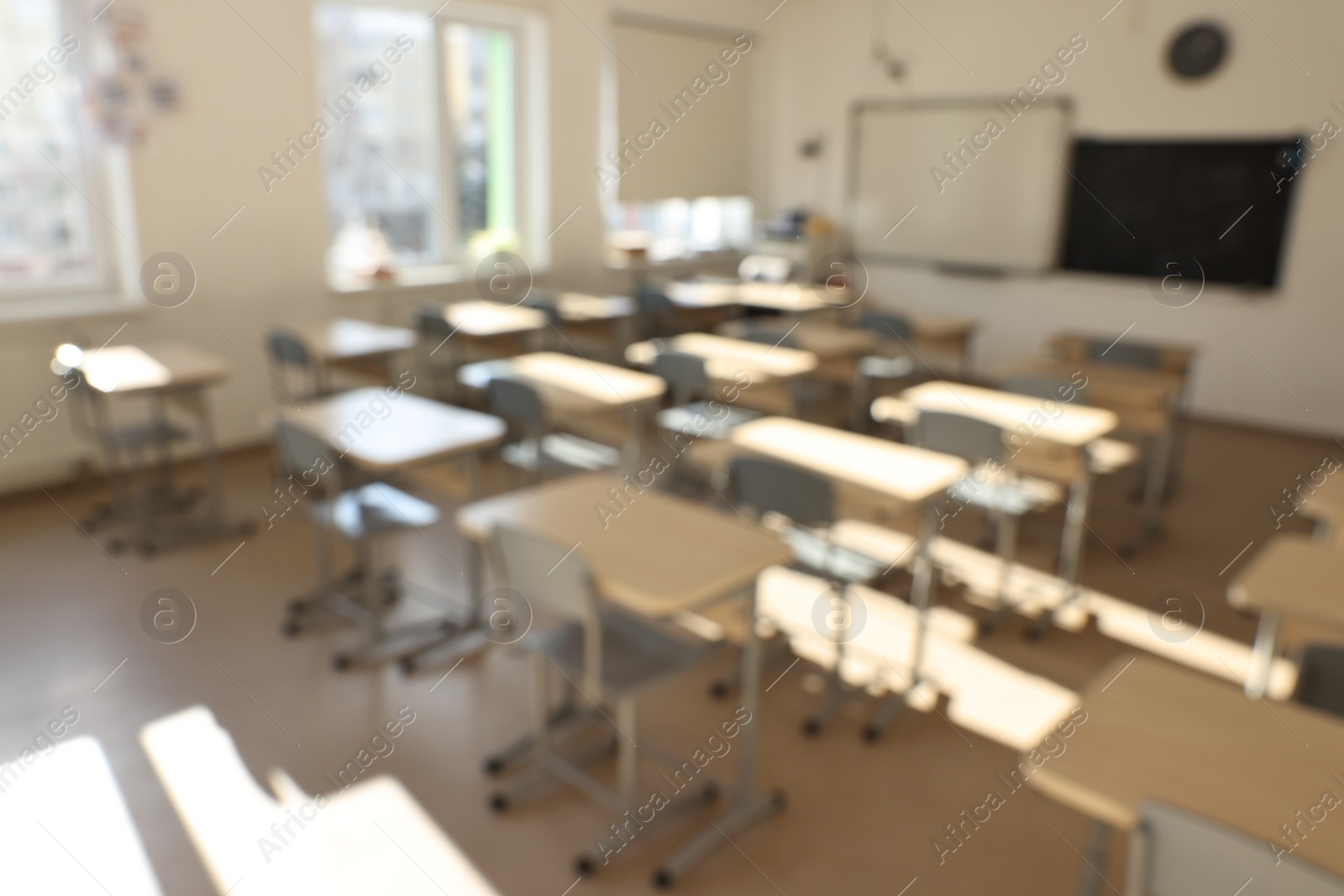 Photo of Blurred view of empty school classroom with desks, windows and chairs