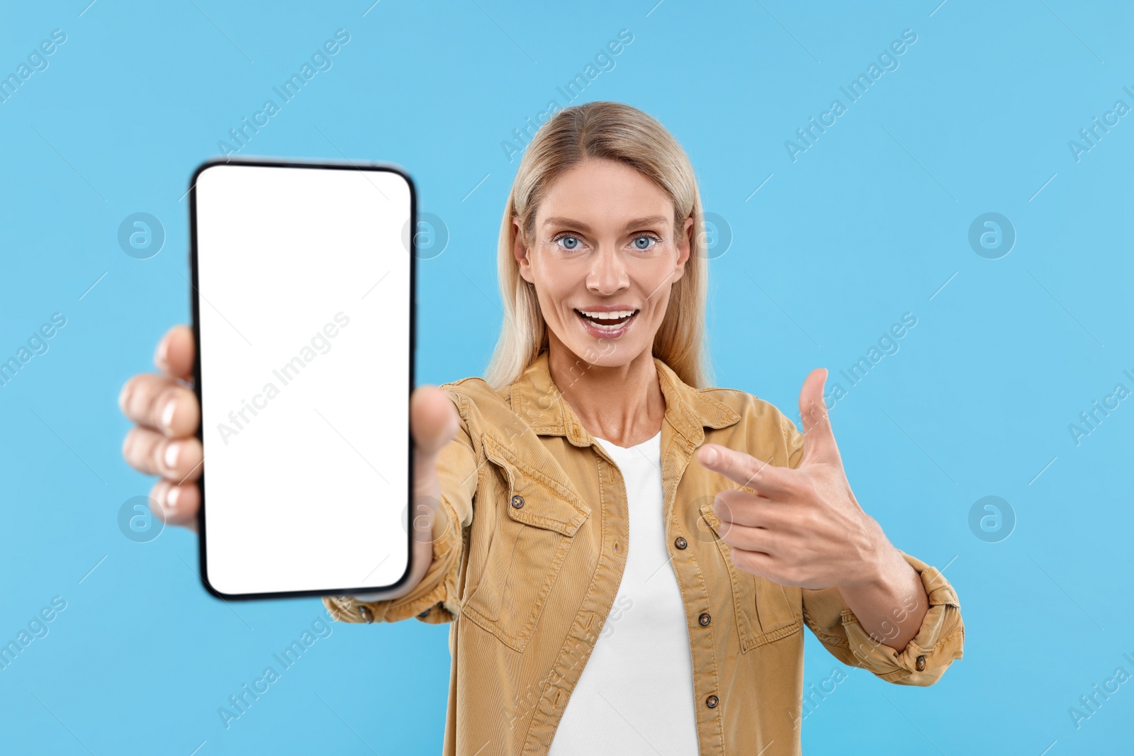 Photo of Happy woman holding smartphone and pointing at blank screen on light blue background