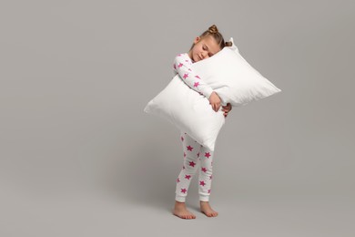 Girl in pajamas hugging pillow on gray background, space for text