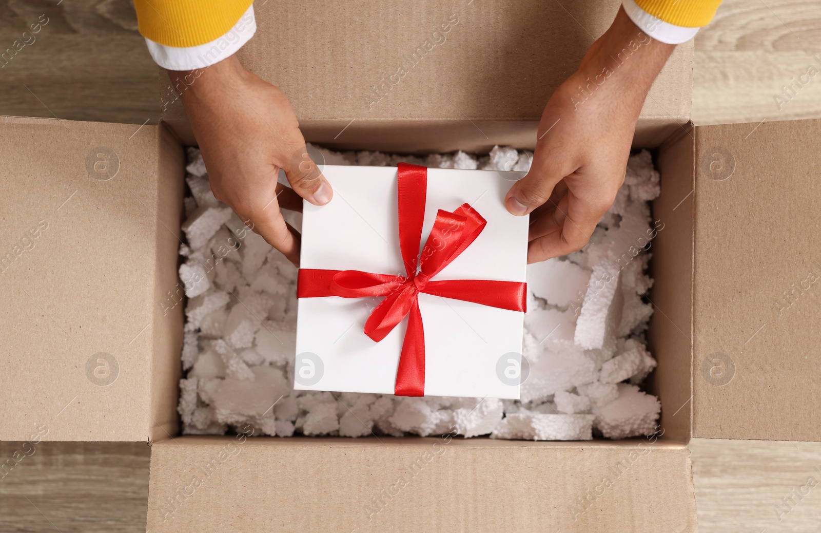 Photo of Man putting Christmas gift box into parcel at wooden table, top view. Sending present by mail