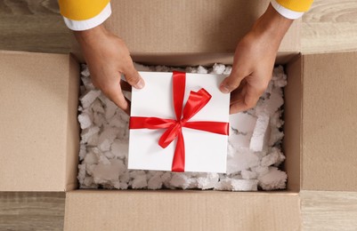 Photo of Man putting Christmas gift box into parcel at wooden table, top view. Sending present by mail