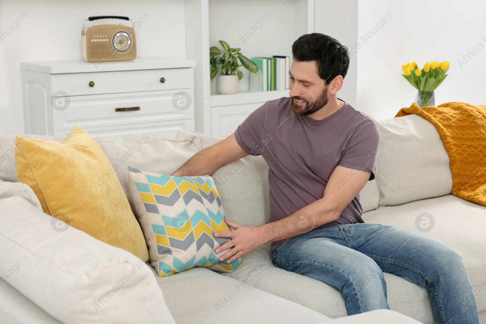 Photo of Spring cleaning. Man putting pillow on sofa in living room