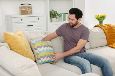 Spring cleaning. Man putting pillow on sofa in living room