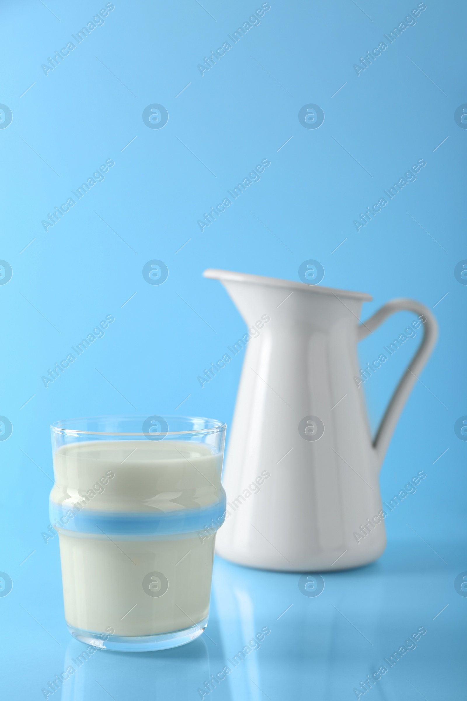 Photo of Glass of fresh milk and jug on light blue background