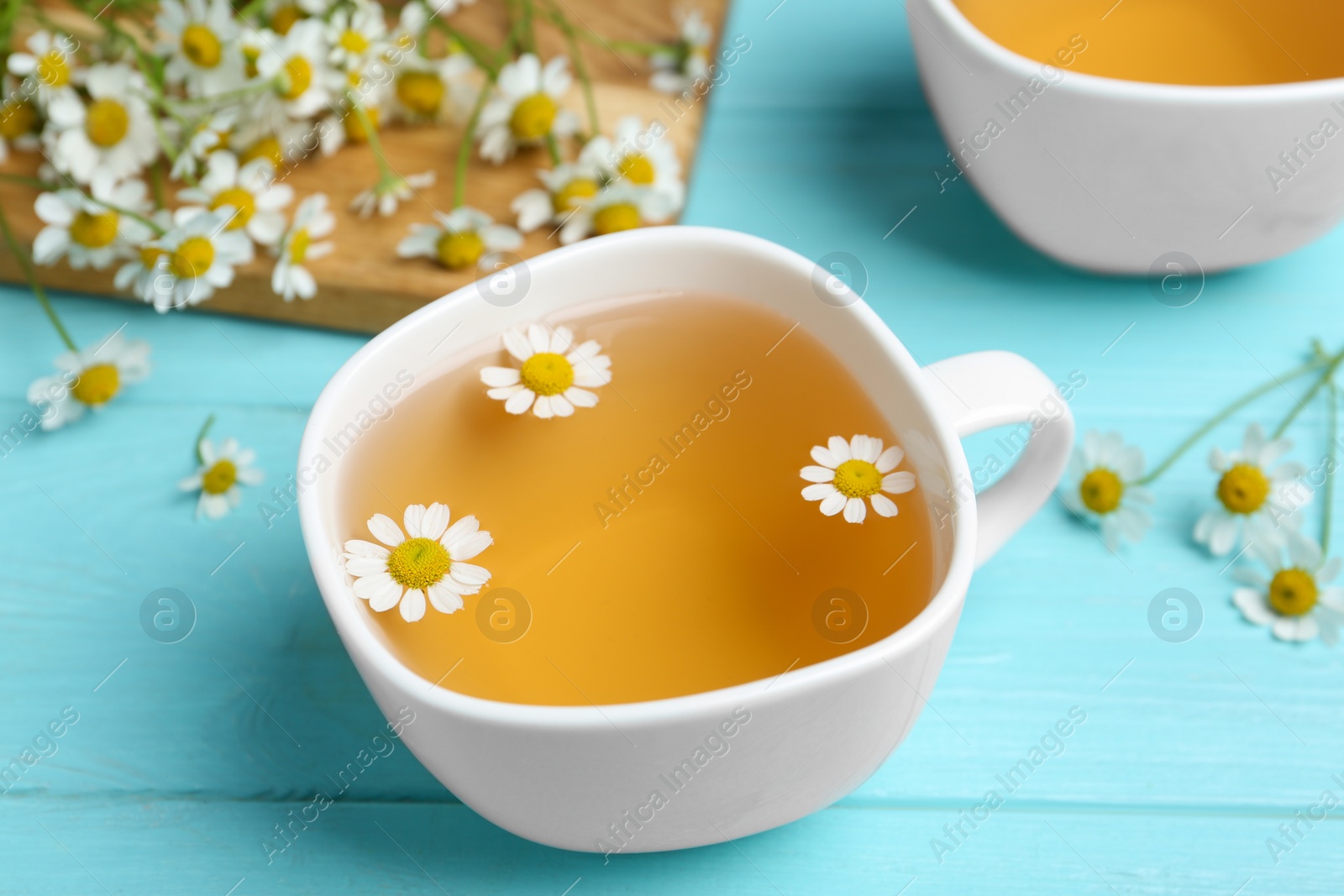 Photo of Fresh chamomile tea in cup on light blue wooden table