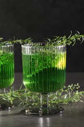 Photo of Glass of homemade refreshing tarragon drink and sprigs on grey table, closeup
