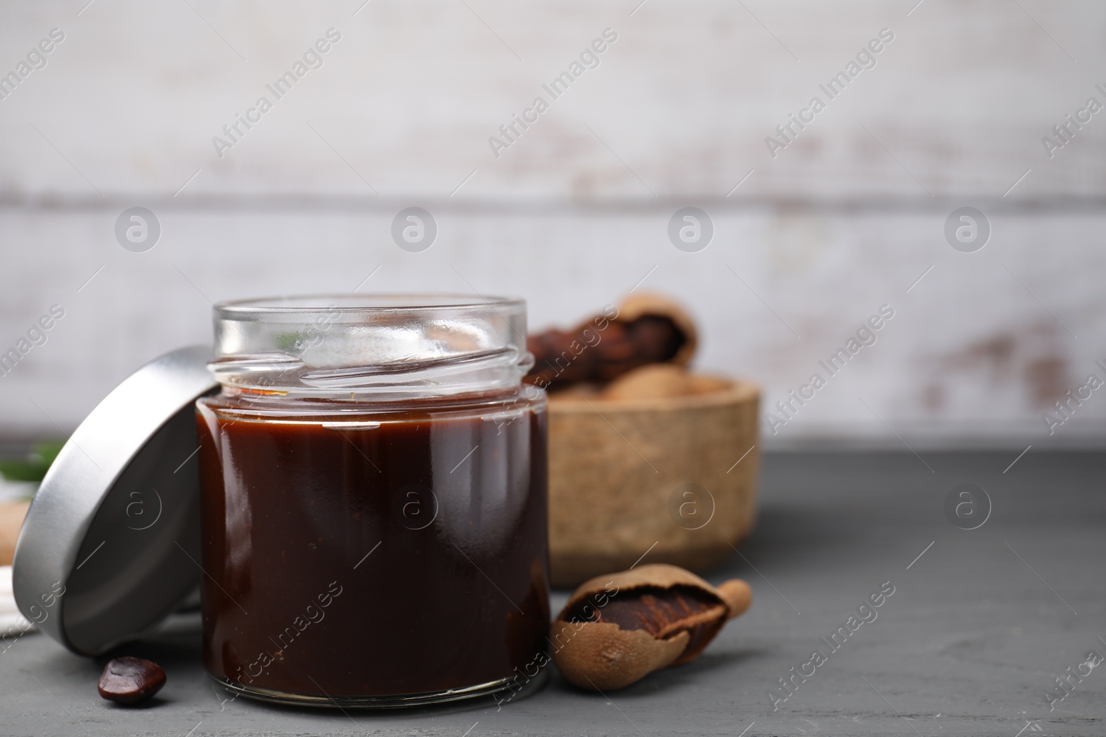 Jar of tasty tamarind sauce and fresh pods on grey wooden table. Space for text Photo of Jar of tasty tamarind sauce and fresh pods on grey wooden table. Space for text
