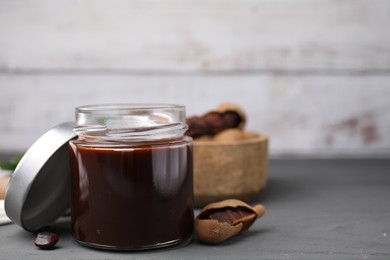 Photo of Jar of tasty tamarind sauce and fresh pods on grey wooden table. Space for text