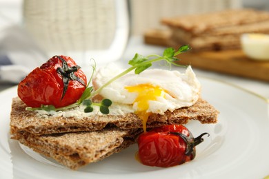 Photo of Fresh rye crispbreads with poached egg, cream cheese and grilled tomatoes on plate, closeup