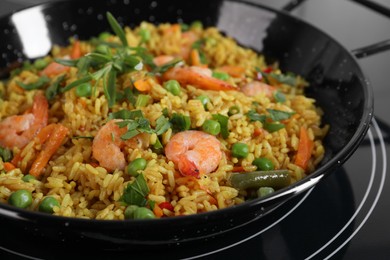 Photo of Tasty rice with shrimps and vegetables in frying pan on induction stove, closeup