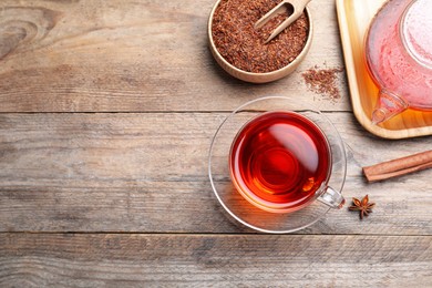 Freshly brewed rooibos tea, scattered dry leaves and spices on wooden table, flat lay. Space for text