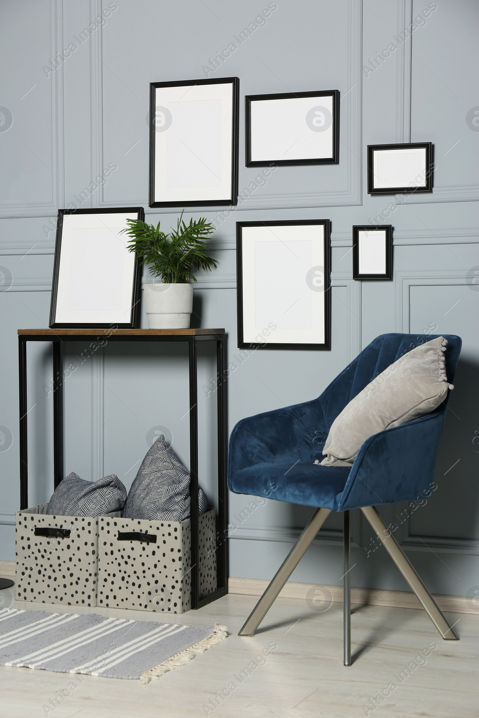 Photo of Stylish room interior with empty frames hanging on grey wall near console table